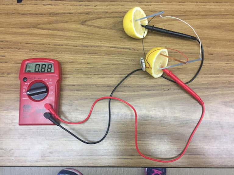 A lemon cut in half with the red probe from a multimeter in one half and the black probe of a multimeter in the other half.