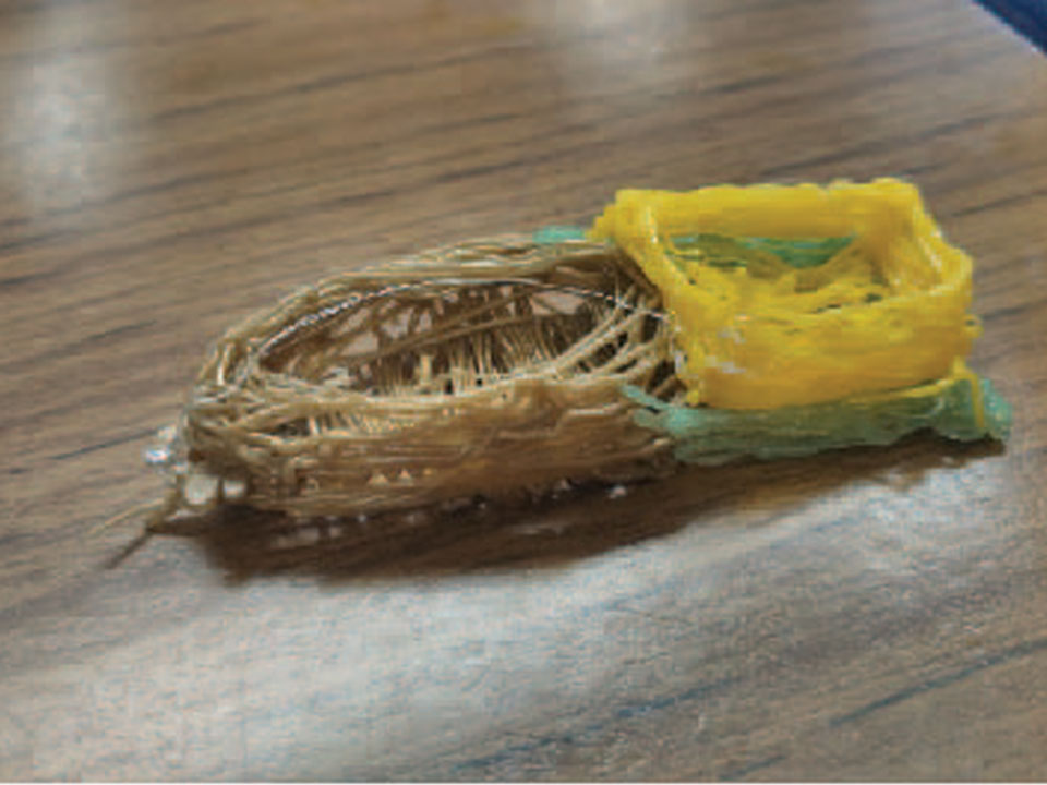 A model made with a 3D pen. On the left is an oval made with tan filament with sides raised. Attached to the right is a square in light green filament and yellow walls that come up off the light green square.