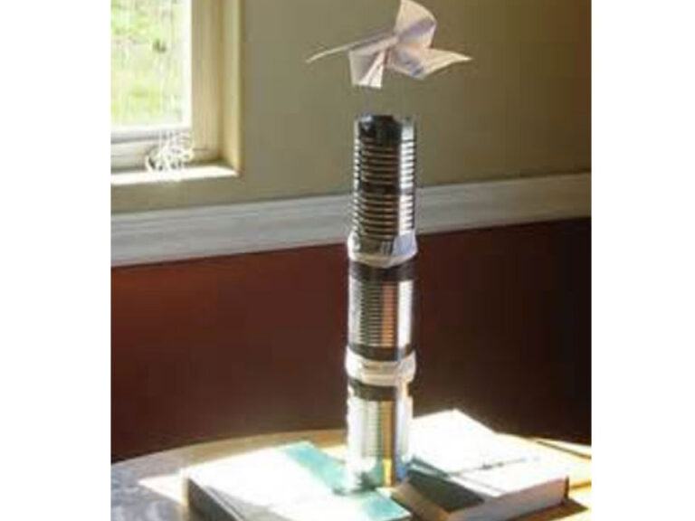 A photo with paper pinwheel floating over a tower of 3 tin cans that are taped together. The cans are supported by two thick text books that are separated by ~2".