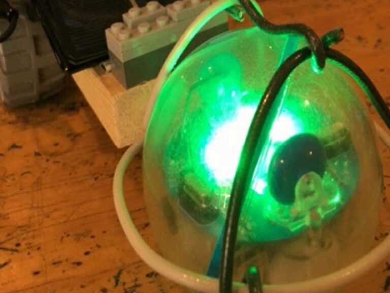 Glowing green spherical robot called a Sphero SPRK+ sitting on a wooden table. Behind it is a small LEGO brick structure.