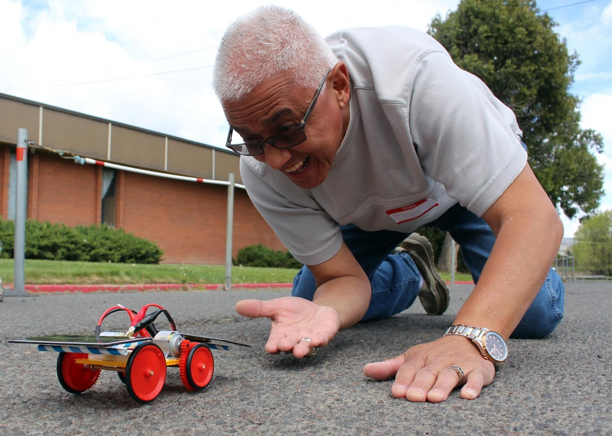 A man kneels on the ground behind a model of a solar car using two solar modules.