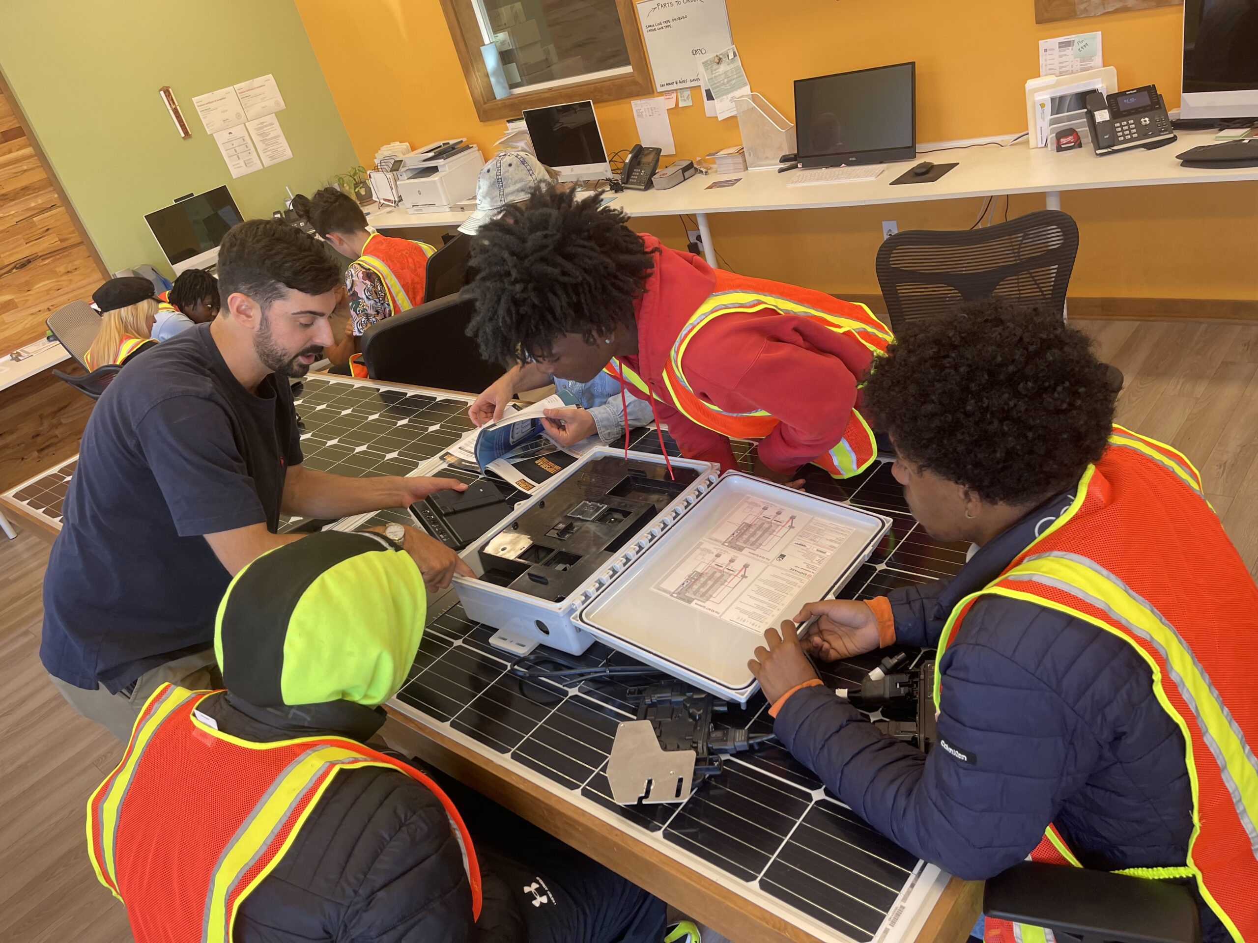 Image of 3 young men and one mentor looking into a white plastic case on top of a solar panel.