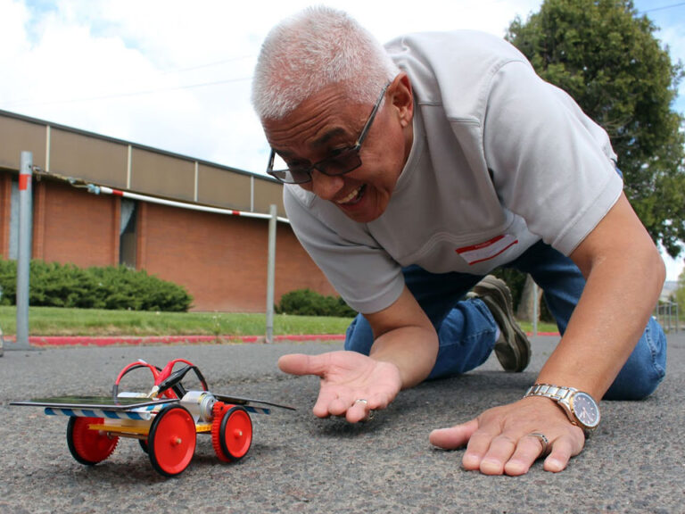 Man kneels on the ground with a solar car model.