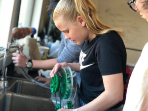 A girl uses a Power Wheel with a hose connected to a sink faucet. 