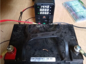 A car battery connected to an inverter. The inverter reads 14.40 V 0.000 A 000.0 W