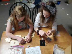 2 girls sit at a table with laser cut model they are assembling. They have a solar module to go with the kit.